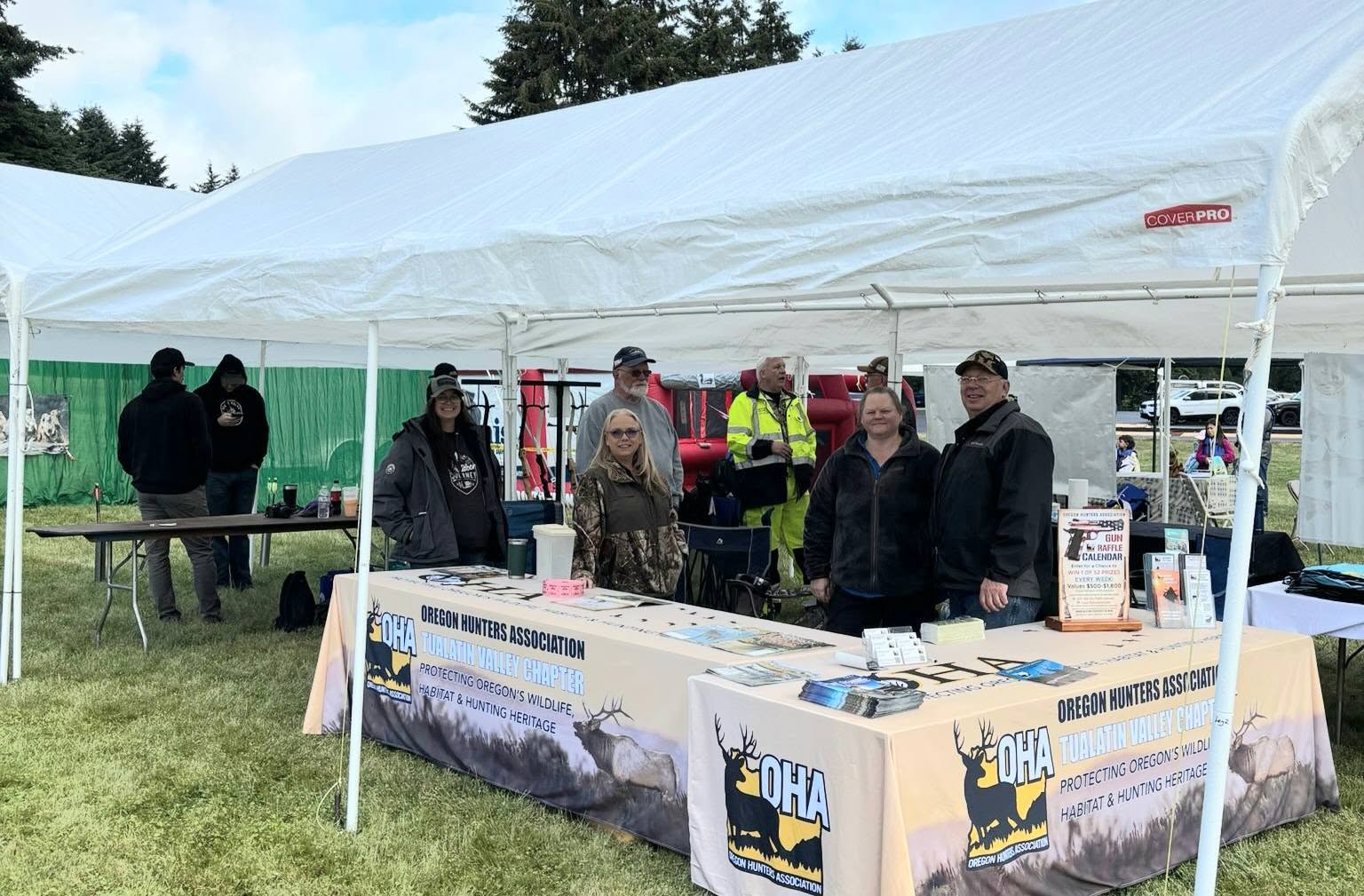 People standing at a booth under a white canopy tent at an outdoor event.