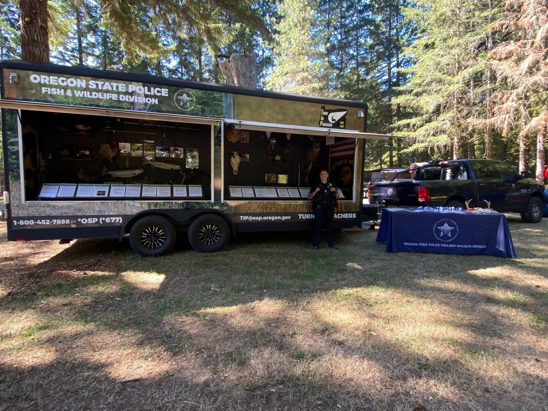 Oregon State Parks outreach trailer beside blue table in a wooded park setting