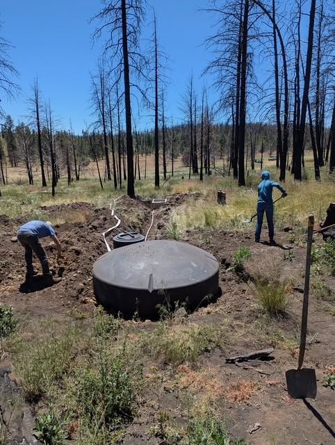 Two people working in a burned forest beside a large black circular tank.