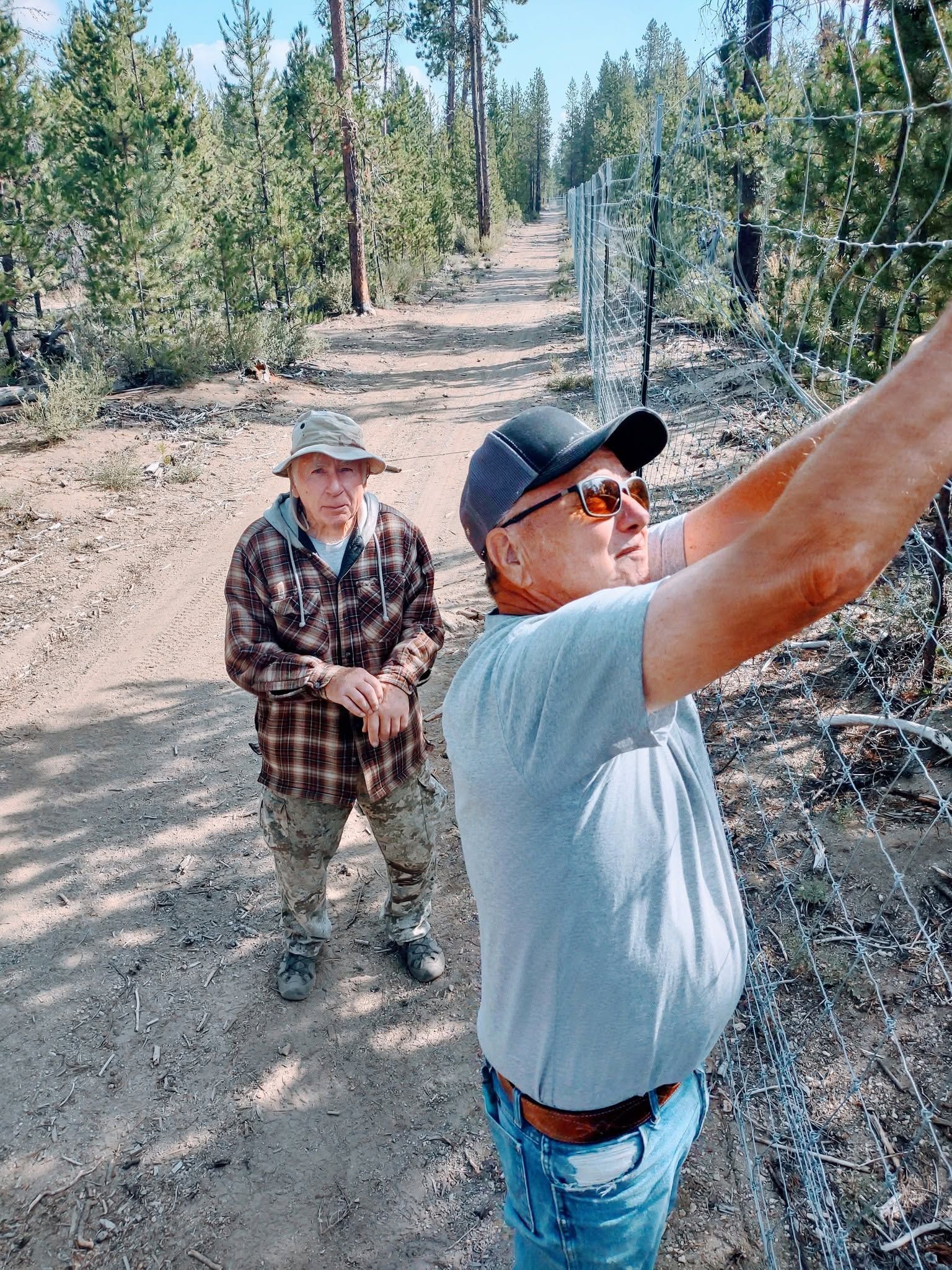 Two hikers on a forest trail, one pointing ahead while the other stands behind.