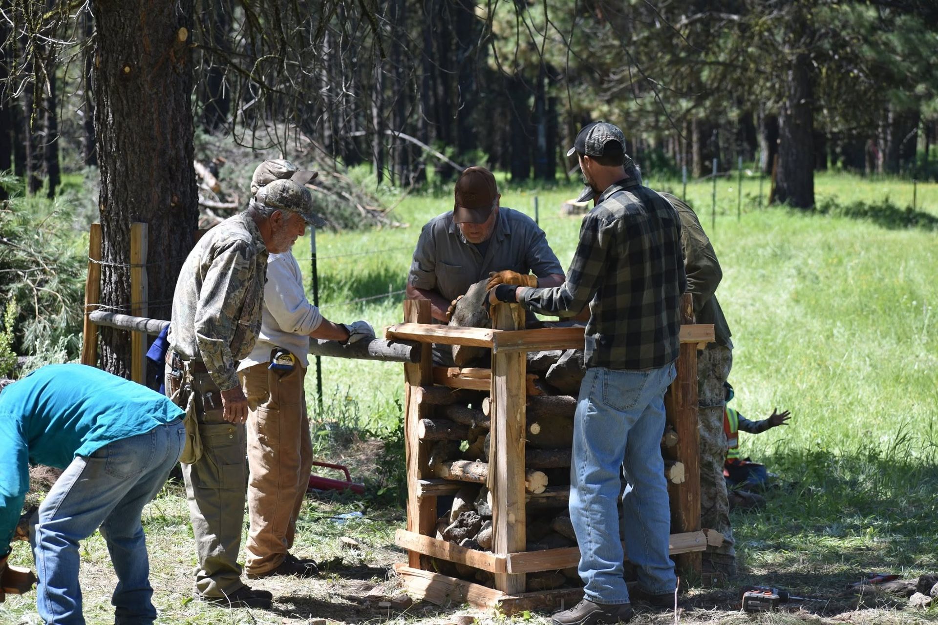 People gathered around a wooden outdoor worktable in a forest clearing.