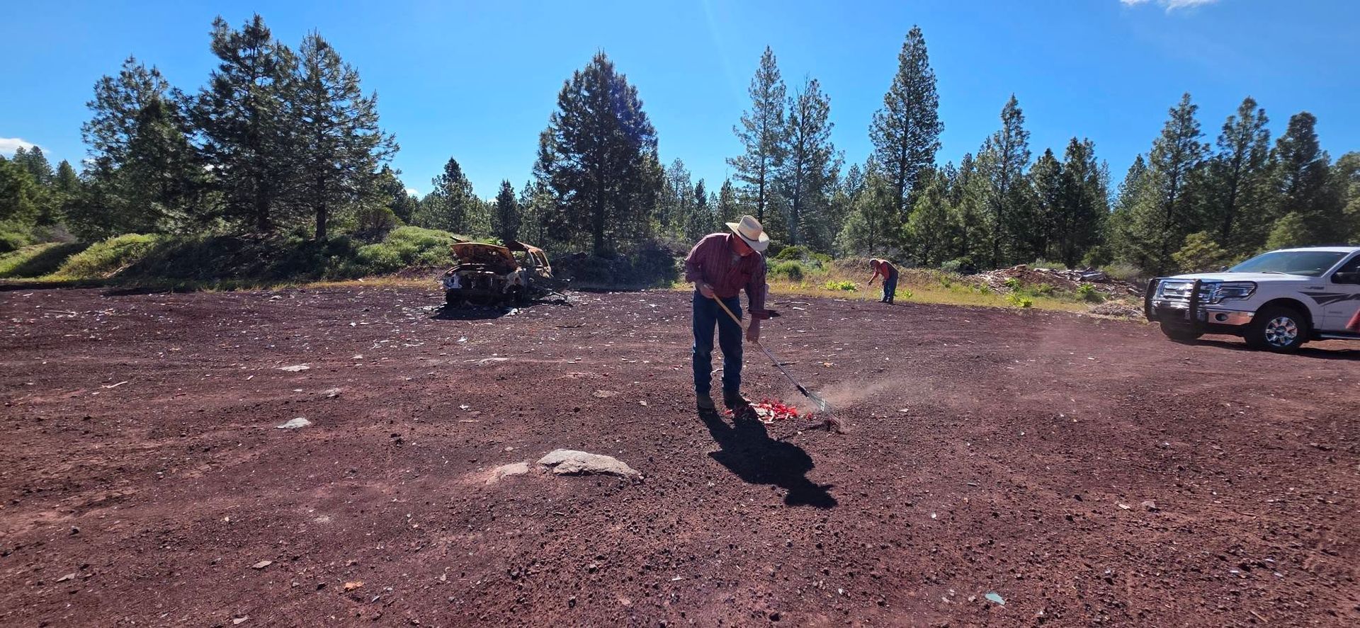 Person standing in a dirt lot with trees and parked cars in the background