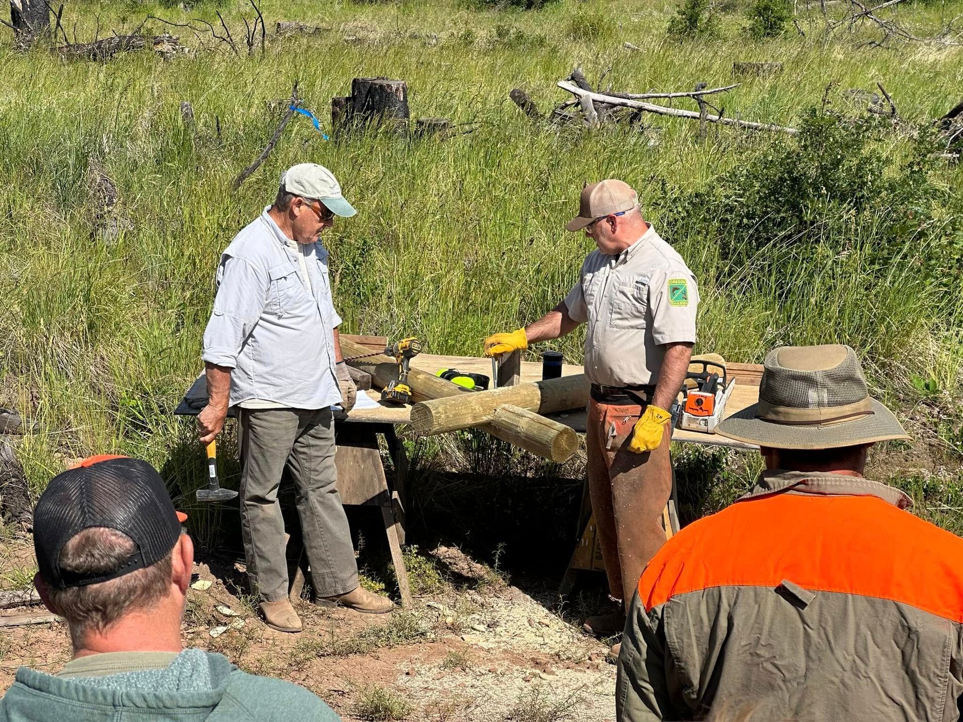 Two park rangers inspect a large animal carcass in a grassy field with onlookers nearby.