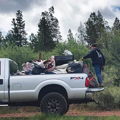 Person loading bags into a silver pickup truck in a wooded area