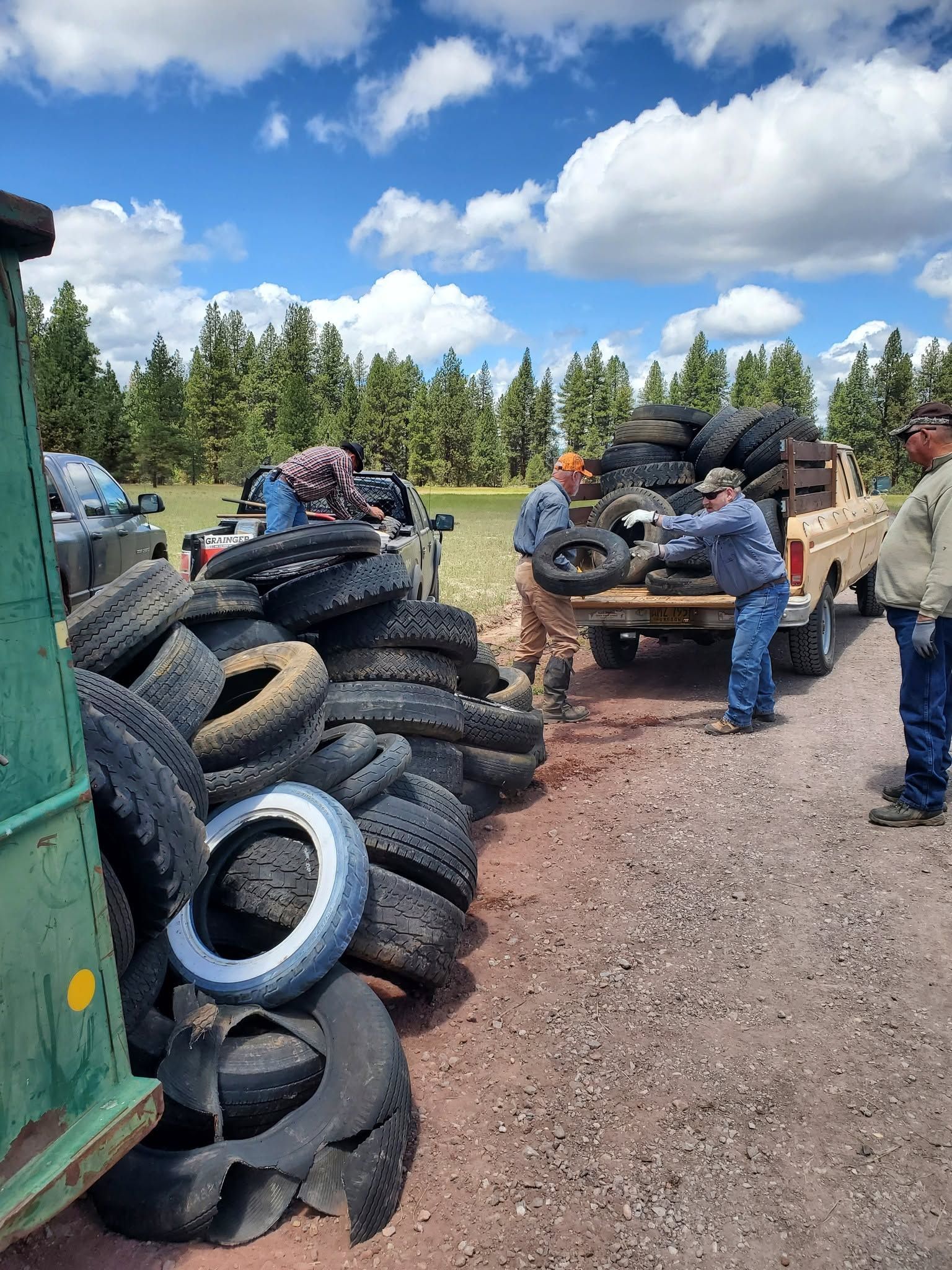 People sorting used tires in a gravel yard with trees and blue sky in the background