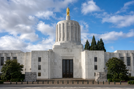 White neoclassical government building with tall central tower, gold statue, and dark entrance under a blue sky