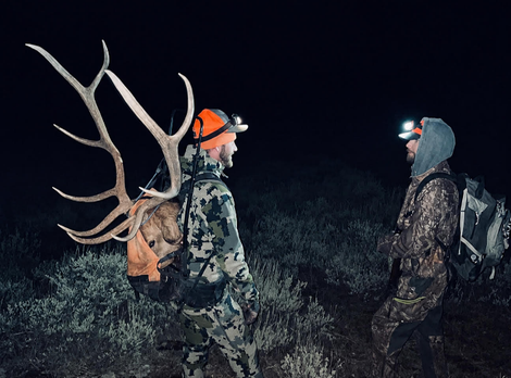 Two hunters with headlamps and antlers on a backpack standing in a dark field at night