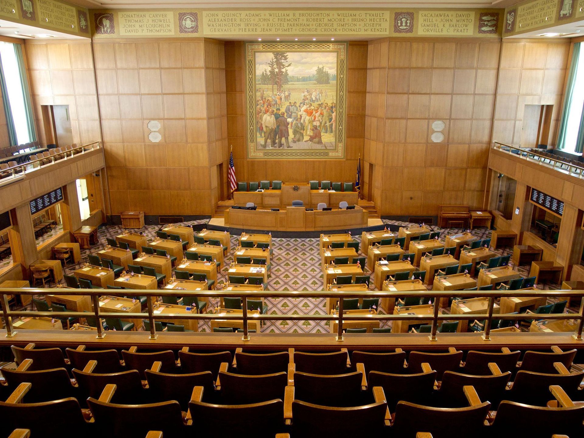 Empty courtroom with wooden desks, American flag, and seal on the wall.