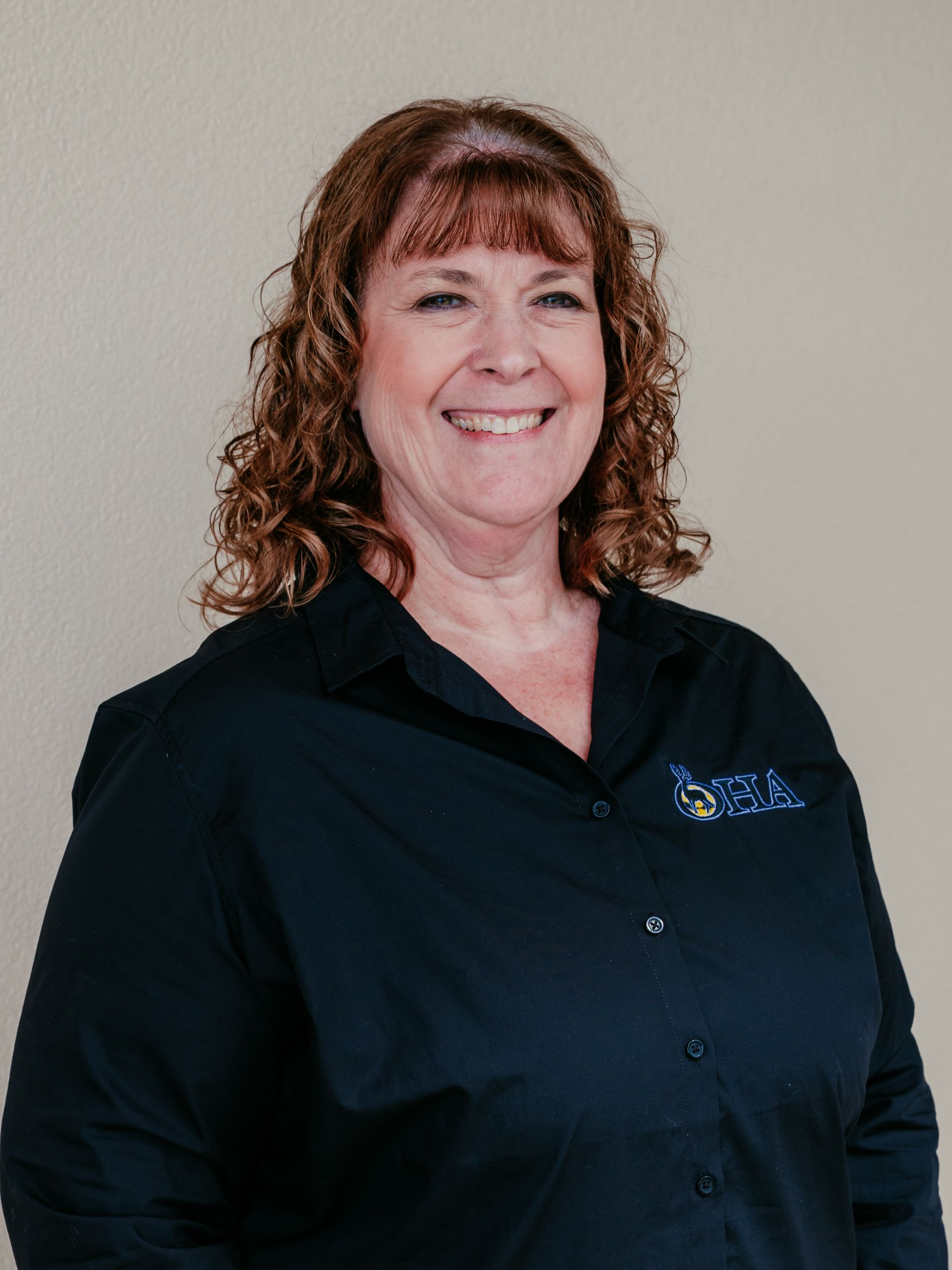 Smiling woman in a black button-up shirt against a plain light background.