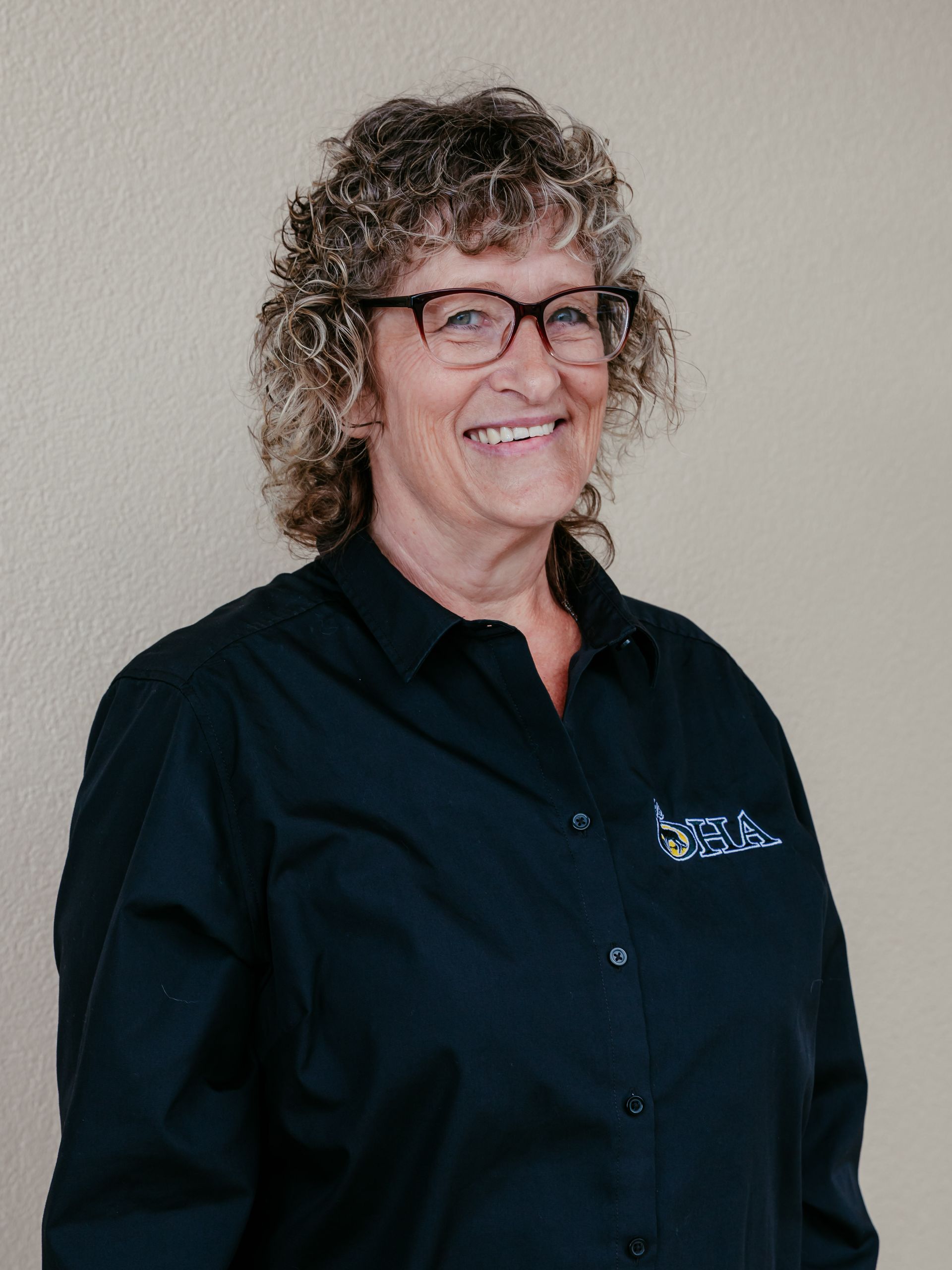 Smiling person in glasses and a black shirt against a beige wall
