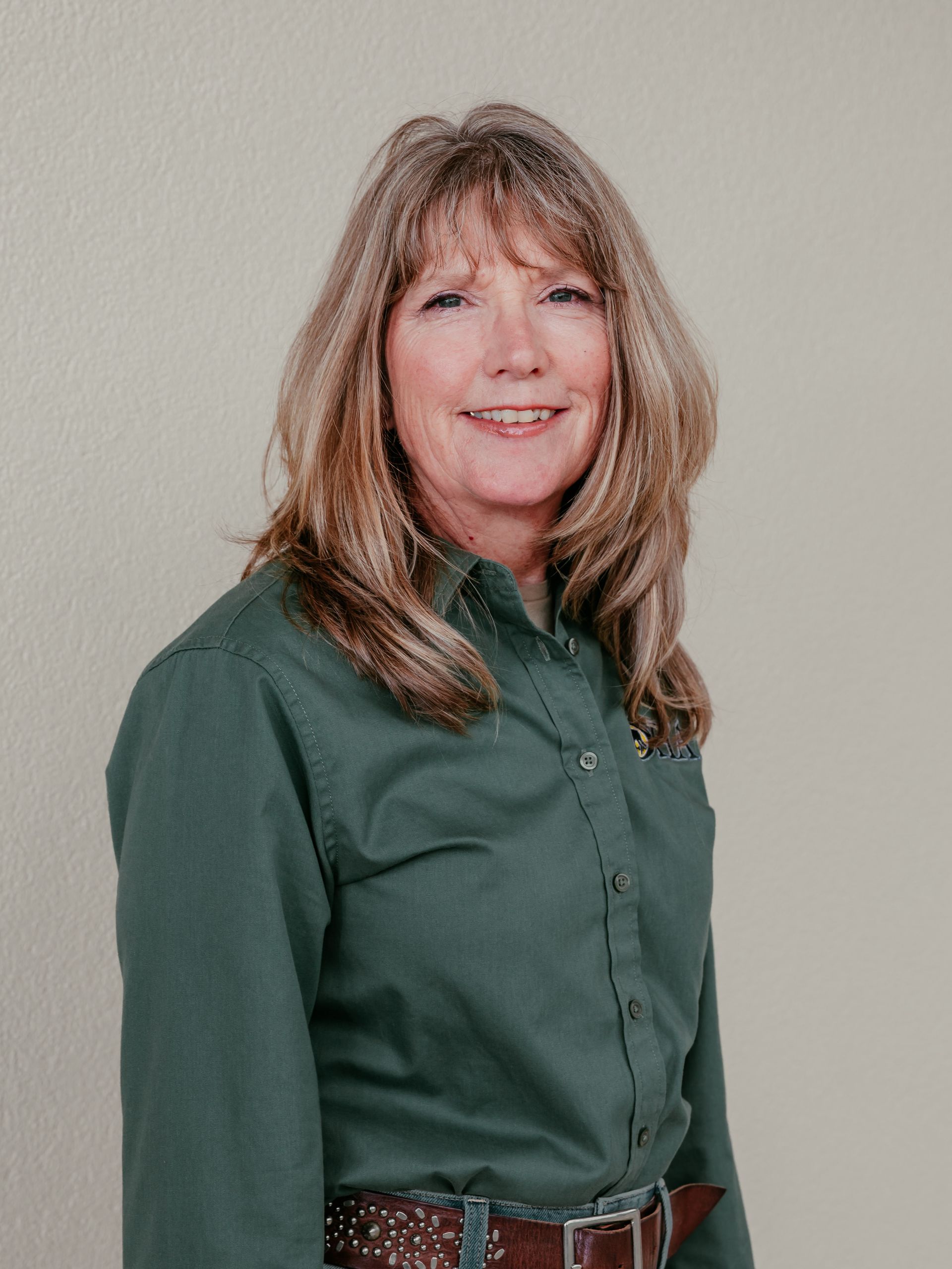 Portrait of a smiling woman in a green button-up shirt against a light background