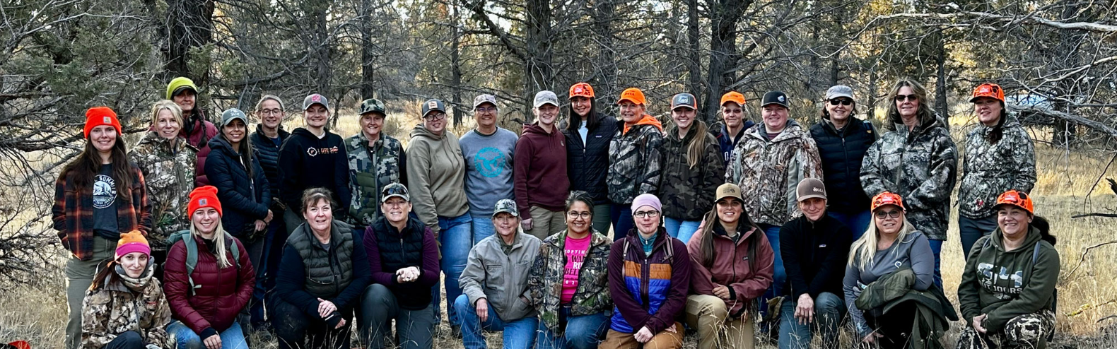 Group of hikers posing outdoors in helmets and outdoor gear, seated and standing in front of rocky terrain.