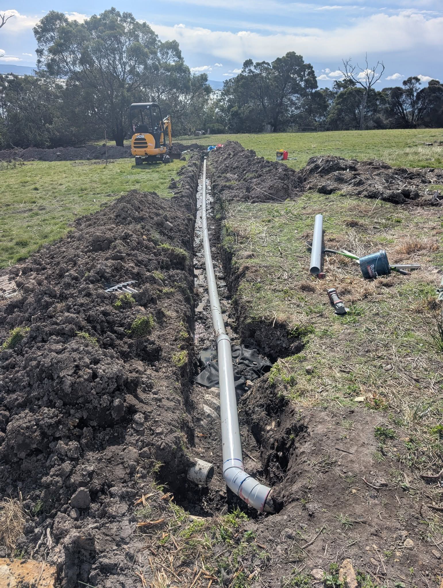 A Gray Pipe Runs Along an Excavated Trench in a Grassy Field — TasWide Plumbing in Kingston, TAS