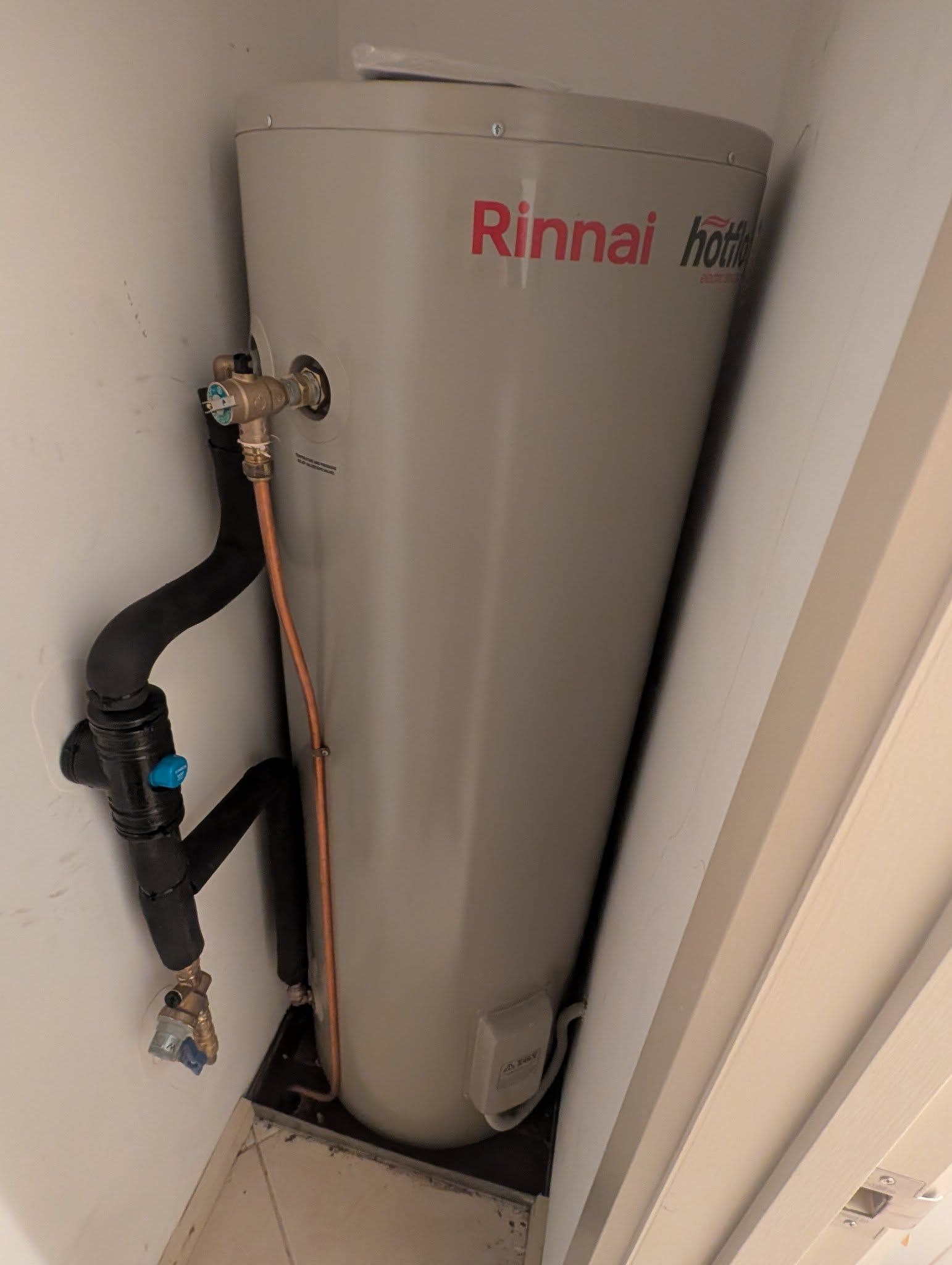 A Gray Cylindrical Water Heater Installed in a Small Indoor Corner — TasWide Plumbing in Kingston, TAS