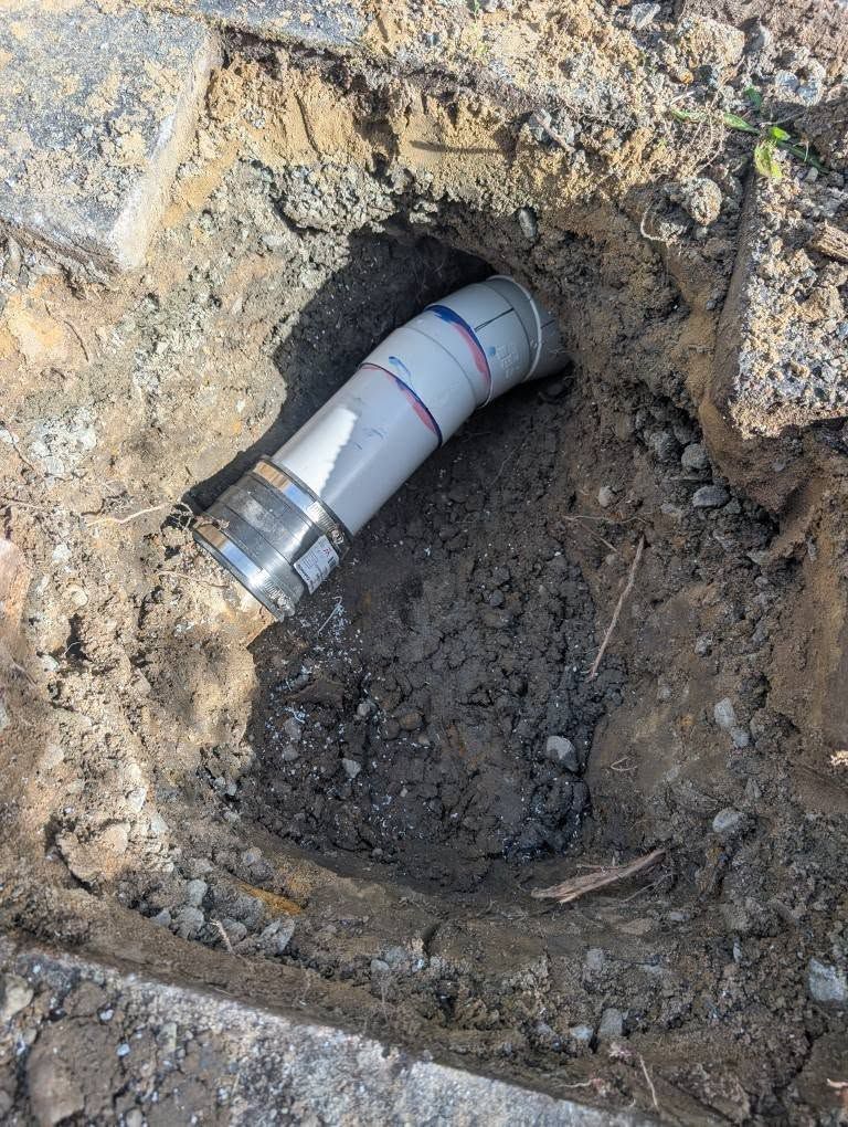 A Gray Plastic Pipe Fitting Connected to a Metal Sleeve in a Hole in the Dirt — TasWide Plumbing in Kingston, TAS