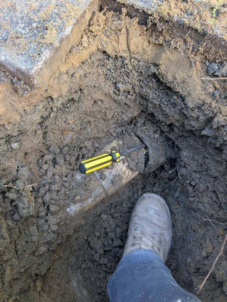 A Yellow-handled Screwdriver Rests on a Pipe in a Dirt Trench — TasWide Plumbing in Kingston, TAS