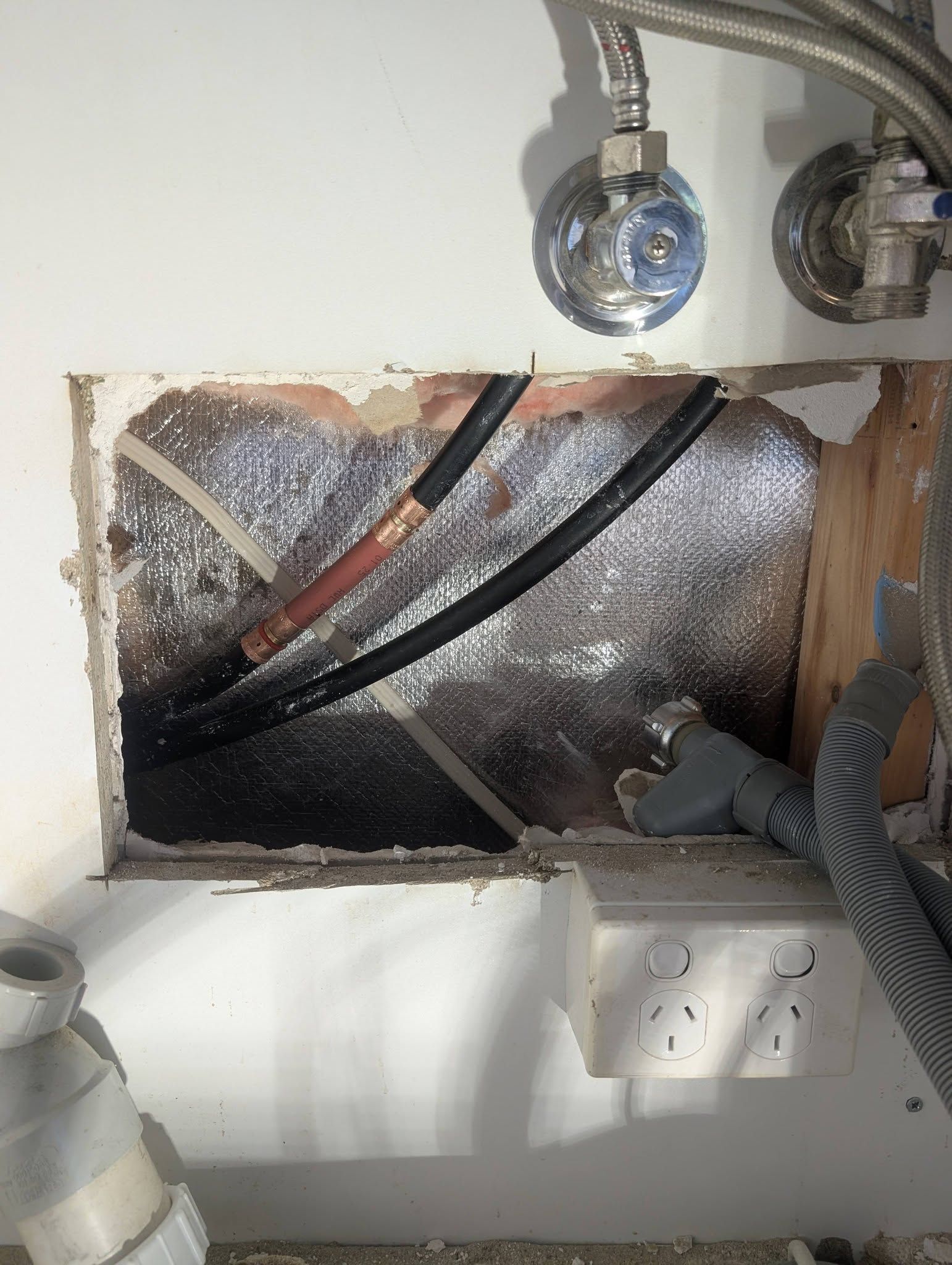 A Rectangular Hole in a White Wall Reveals Exposed Pipes — TasWide Plumbing in Kingston, TAS