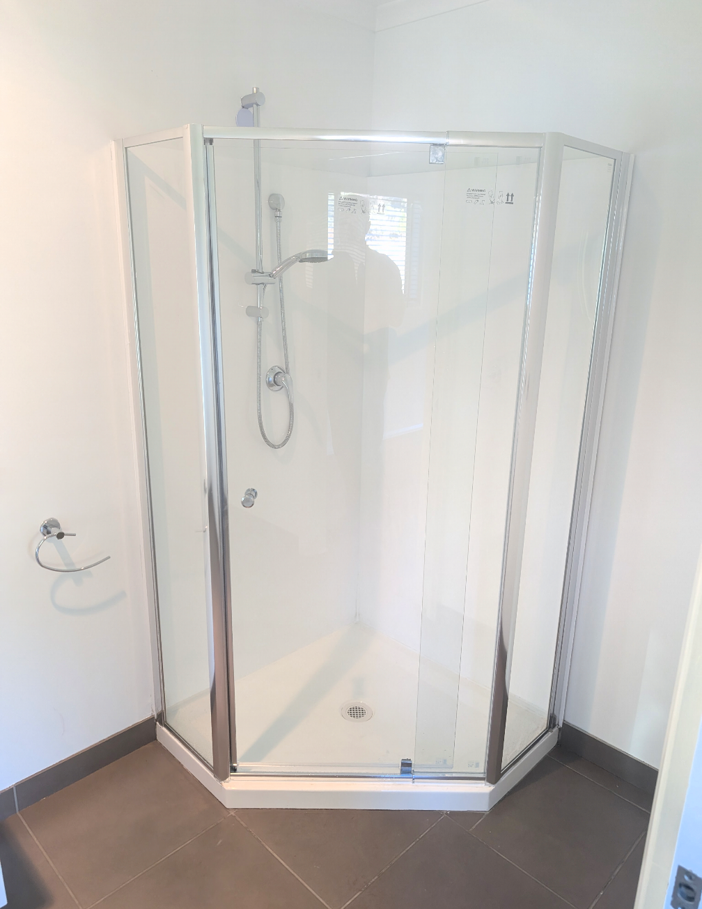 Glass corner shower stall in a bathroom with white walls and dark tile floor — TasWide Plumbing in Kingston, TAS