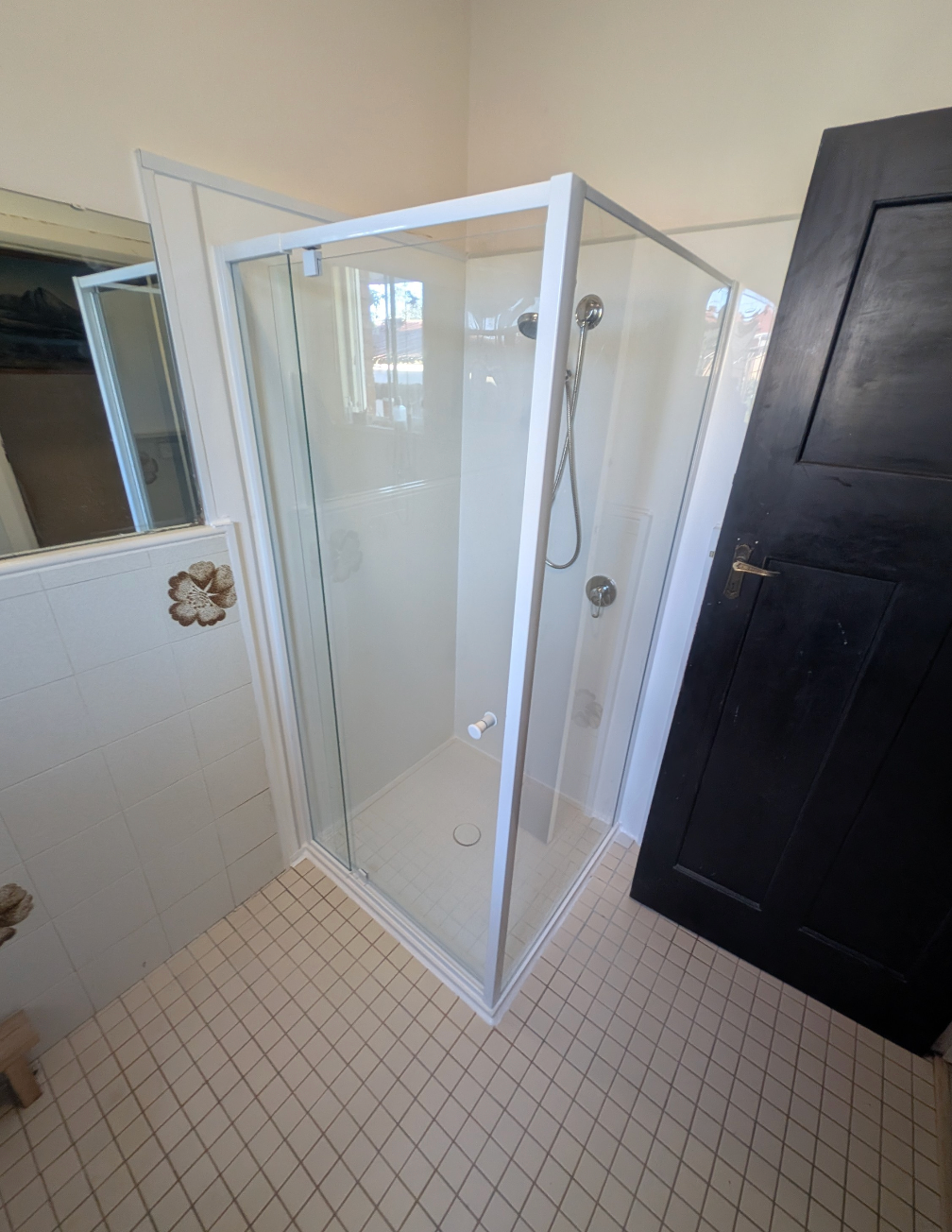 Small bathroom with a glass shower stall, white tile floor, mirror, and black door— TasWide Plumbing in Kingston, TAS