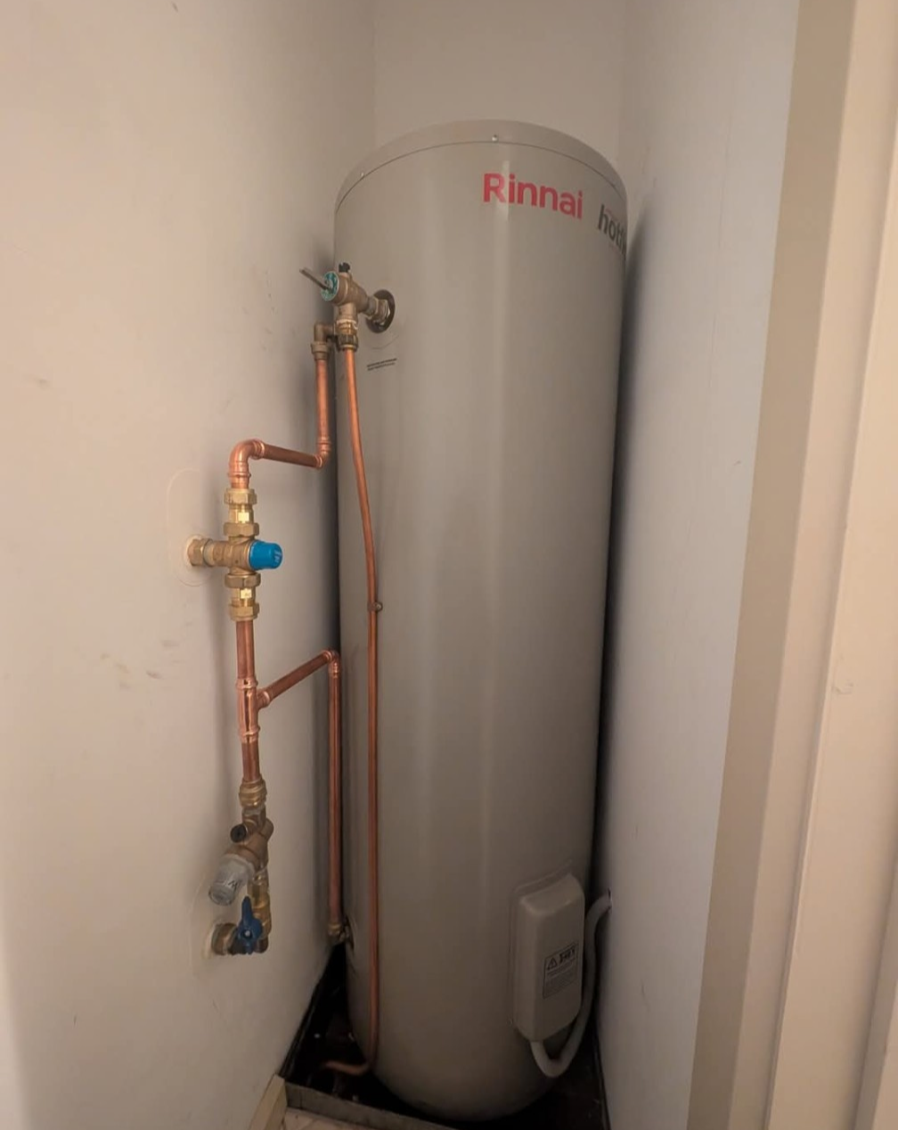 Tall gray Rinnai water heater with exposed copper pipes in a narrow utility closet — TasWide Plumbing in Kingston, TAS
