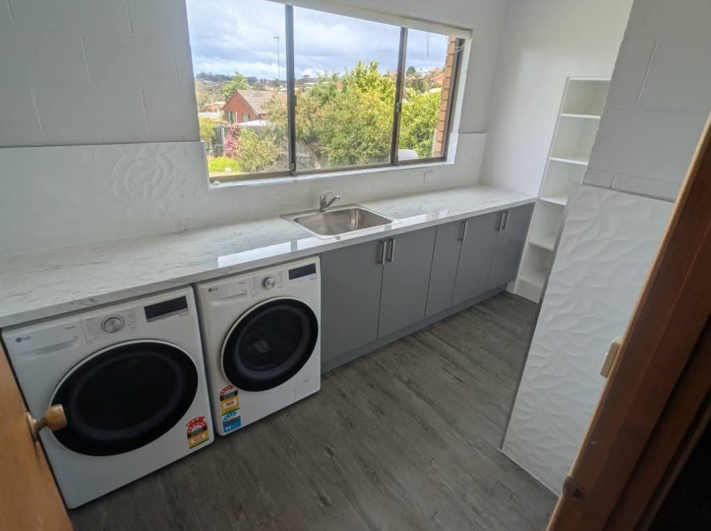 Laundry room with washer and dryer, long countertop, sink, cabinets, and a large window. — TasWide Plumbing in Kingston, TAS