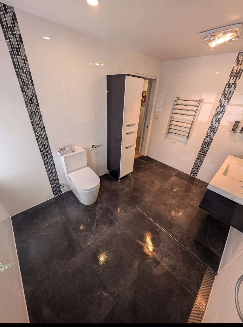 Modern bathroom with white walls, dark tile floor, toilet, vanity, and towel rack — TasWide Plumbing in Kingston, TAS