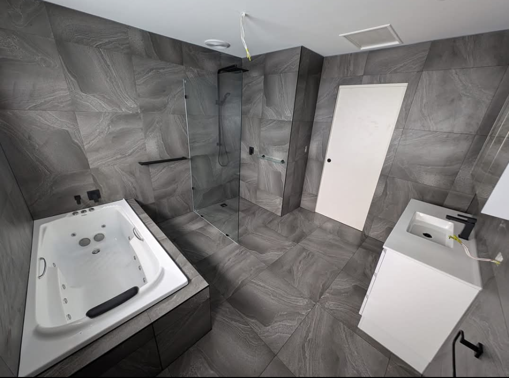 Modern gray-tiled bathroom with a bathtub, vanity sink, and closed white door — TasWide Plumbing in Kingston, TAS