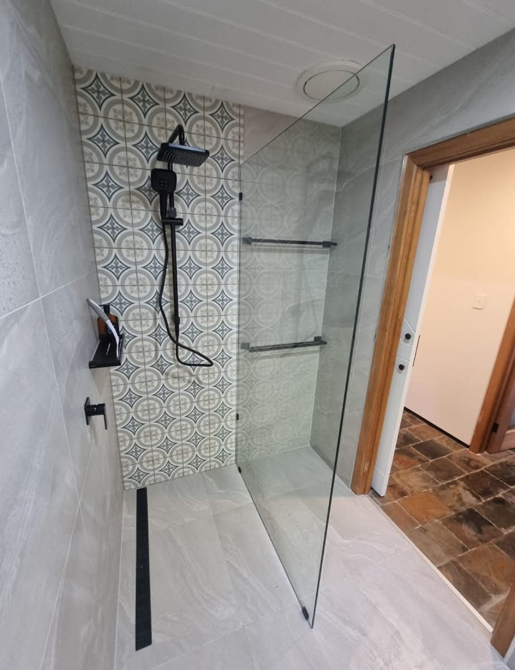 Modern shower stall with glass panel, black fixtures, patterned accent tile, and white floor tiles — TasWide Plumbing in Kingston, TAS