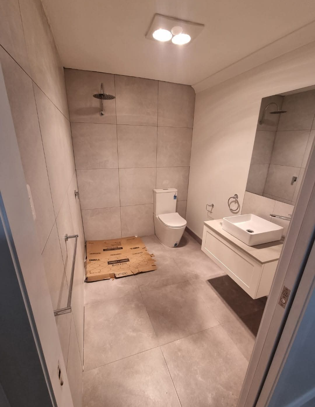 A small bathroom with a glass-enclosed shower, white toilet, and a vanity sink against a light-colored wall. — TasWide Plumbing in Margate, TAS