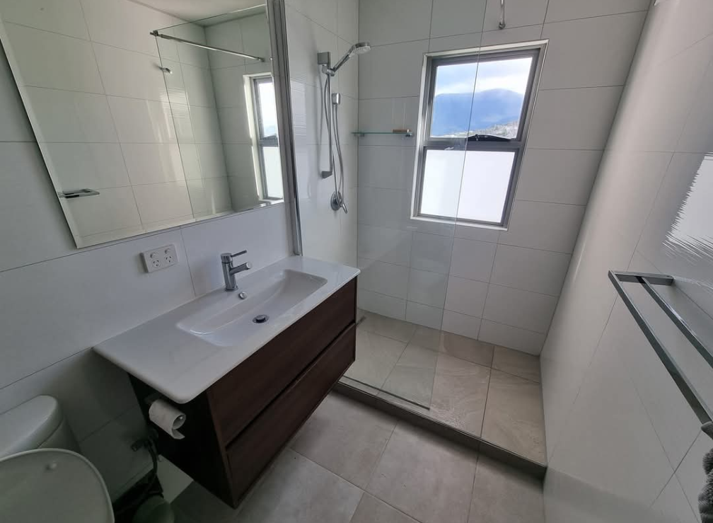 Modern bathroom with white tile, dark vanity, sink, mirror, towel rack, and a window. — TasWide Plumbing in Kingston, TAS