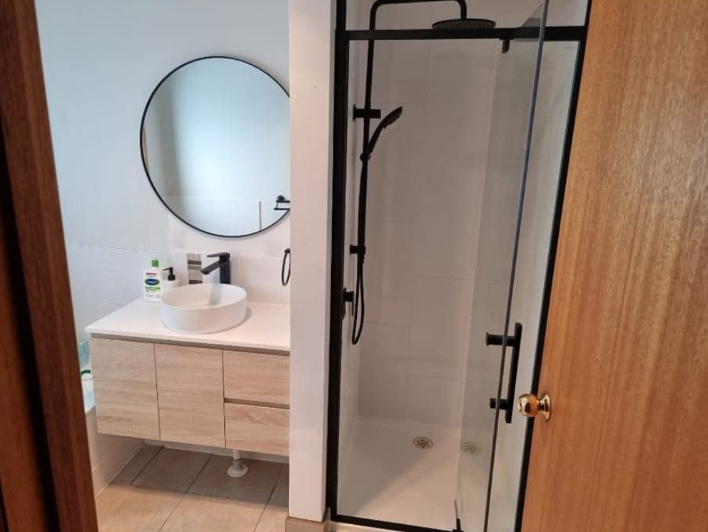 Bathroom vanity and walk-in shower with glass door, round mirror, and light wood cabinet. — TasWide Plumbing in Kingston, TAS