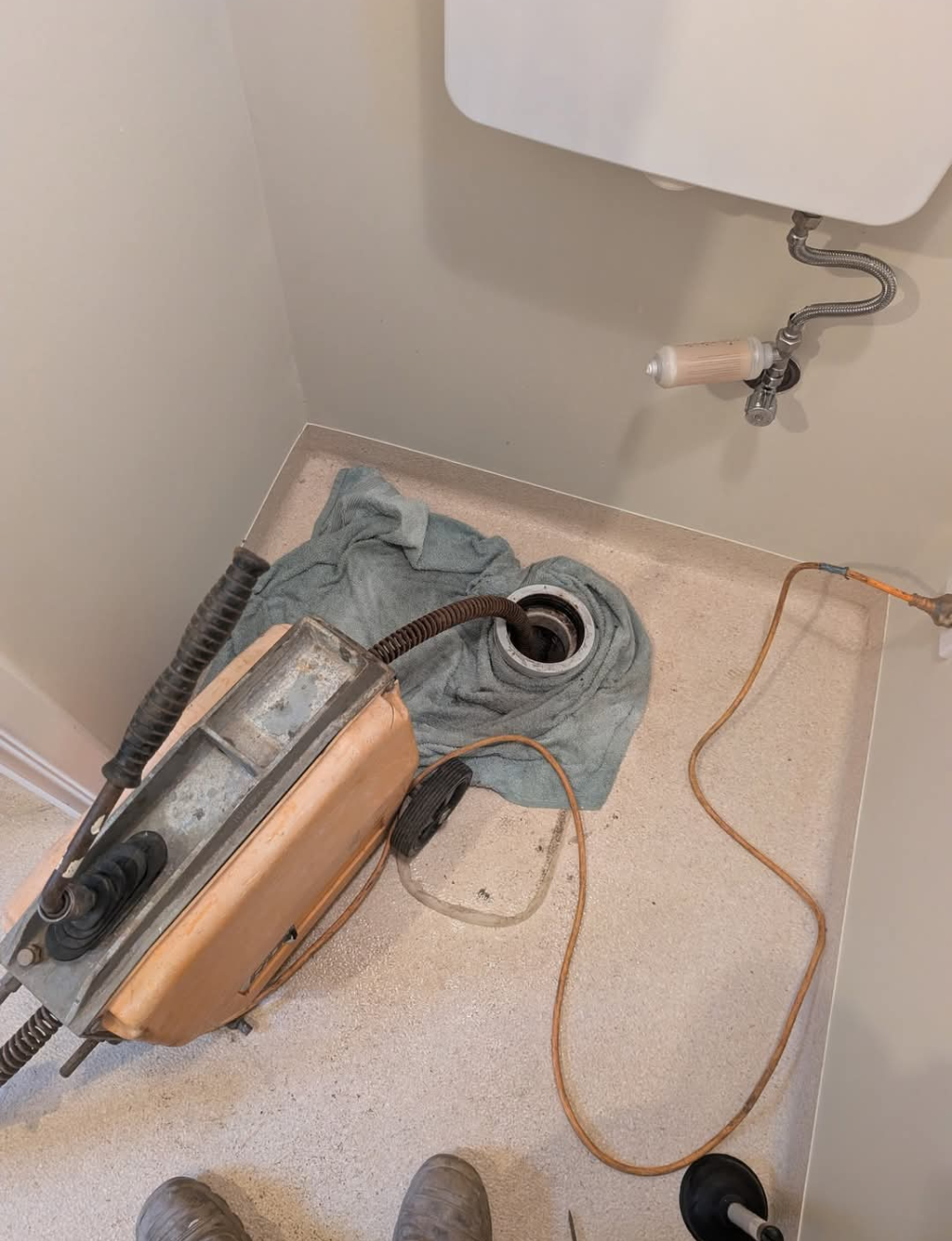 Vacuum cleaner lying on a bathroom floor beside a sink and drain hose — TasWide Plumbing in Kingston, TAS