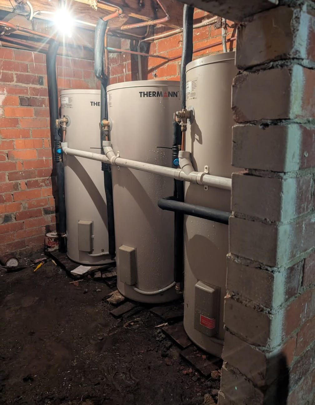 Basement with three white water heaters and exposed pipes against brick walls — TasWide Plumbing in Kingston, TAS