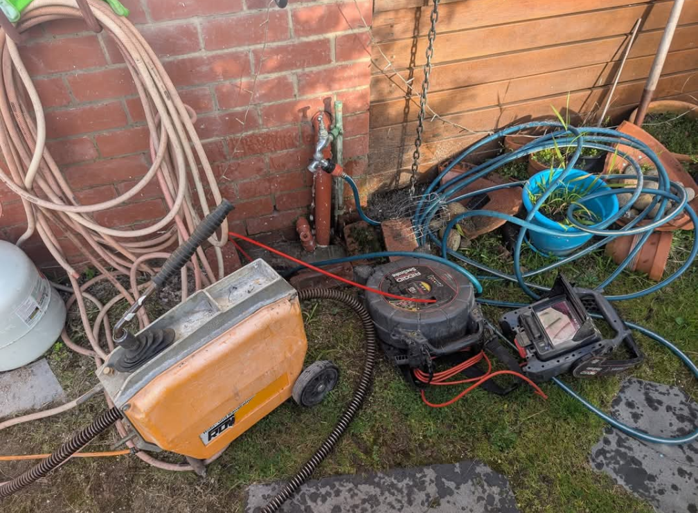 Orange generator and tangled hoses, cables, and tools beside a brick wall outdoors. — TasWide Plumbing in Kingston, TAS