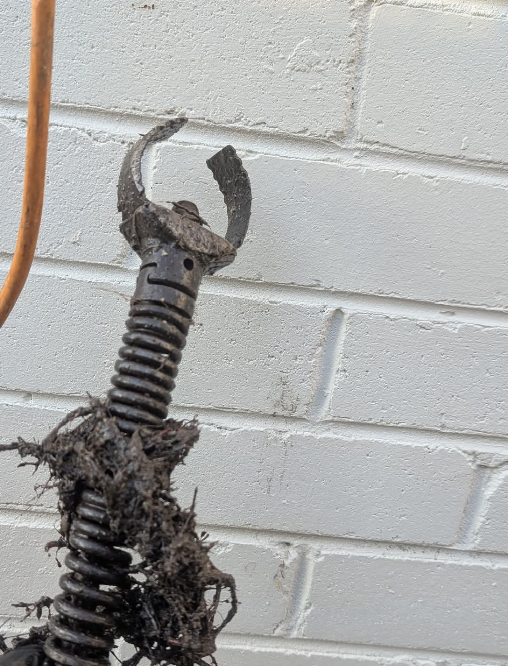 Damaged metal garden tool handle against a white cinderblock wall — TasWide Plumbing in Kingston, TAS