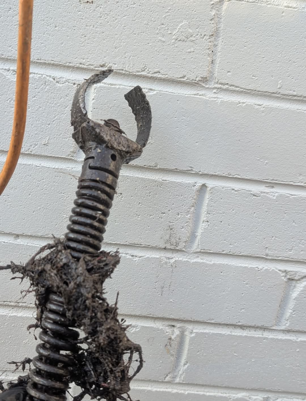 Rusty metal claw tool on a black spring against a white brick wall. — TasWide Plumbing in Kingston, TAS