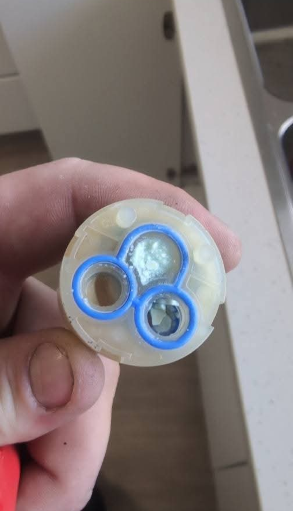 Close-up of a hand holding a small circular plastic part with three blue-ringed openings — TasWide Plumbing in Kingston, TAS