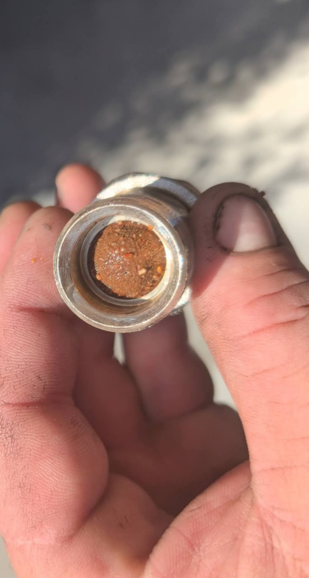 Close-up of a small metal container with a rusty brown substance, held between fingers outdoors. — TasWide Plumbing in Kingston, TAS