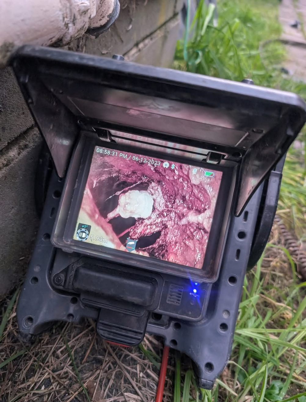 Small monitor in a black hood showing a pinkish scene outdoors on grass, with cables attached — TasWide Plumbing in Kingston, TAS