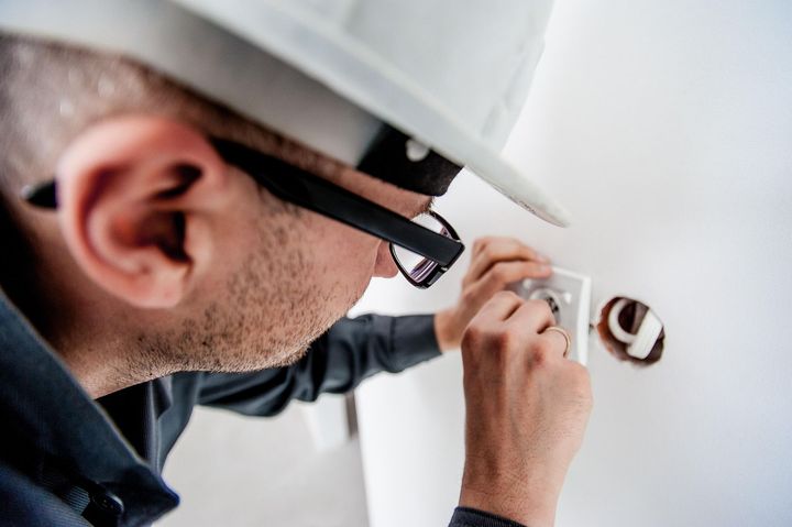 Technician in a hard hat installing wiring on a wall outlet