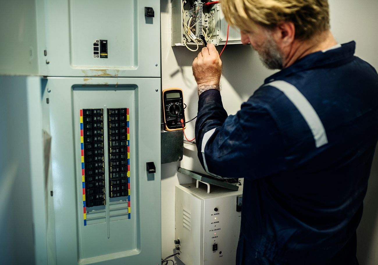 Technician inspecting an open electrical panel and wiring in a utility room