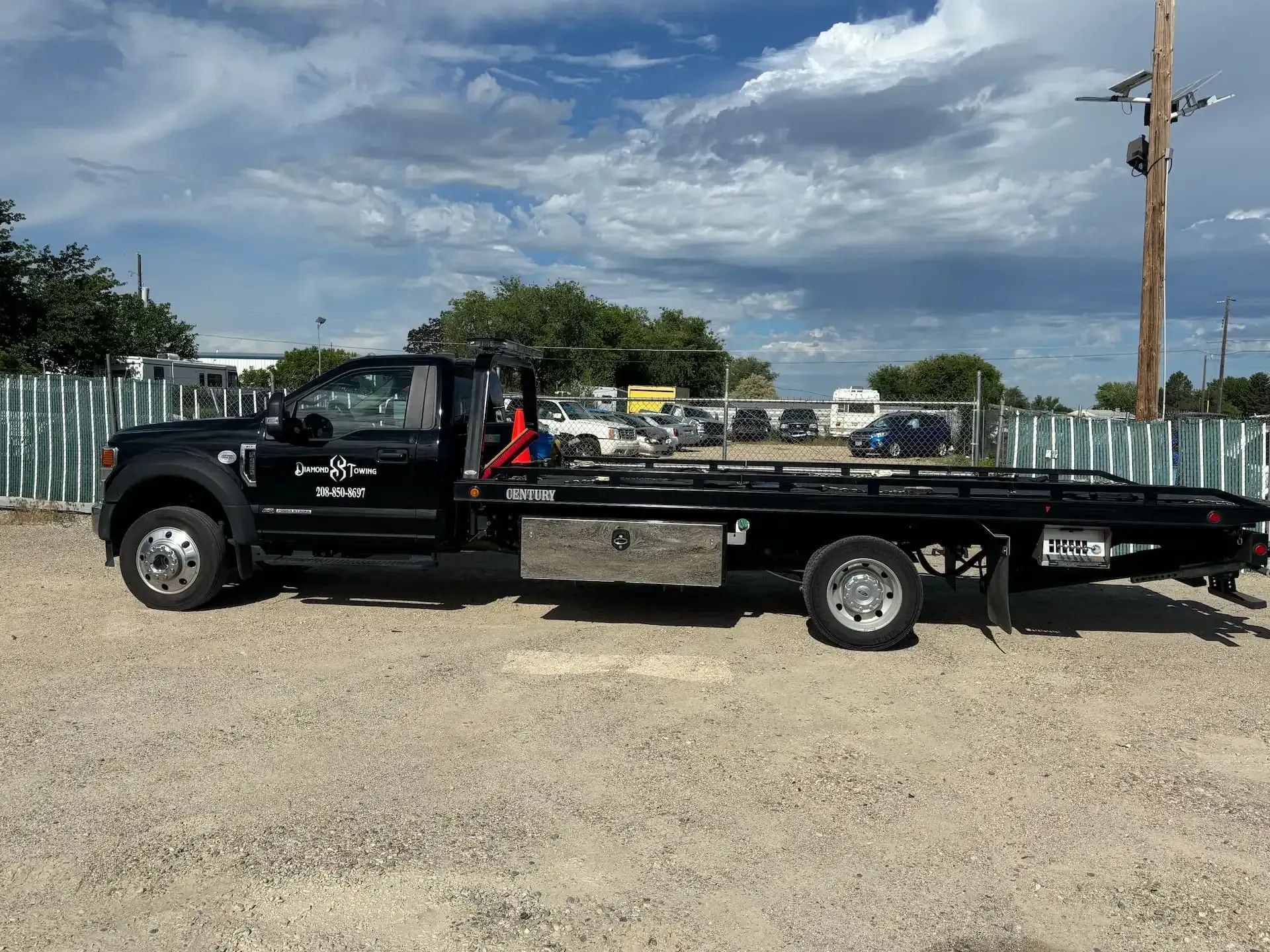 Black flatbed tow truck parked on a gravel lot under a cloudy sky