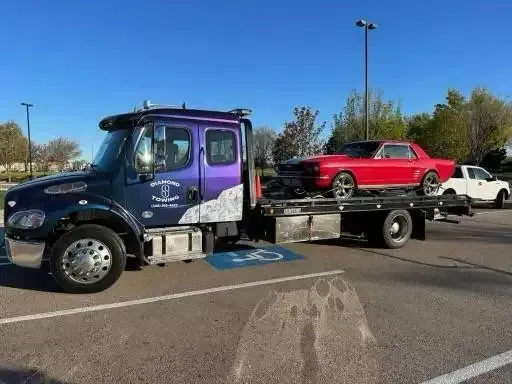 A purple tow truck is towing a red car in a parking lot.