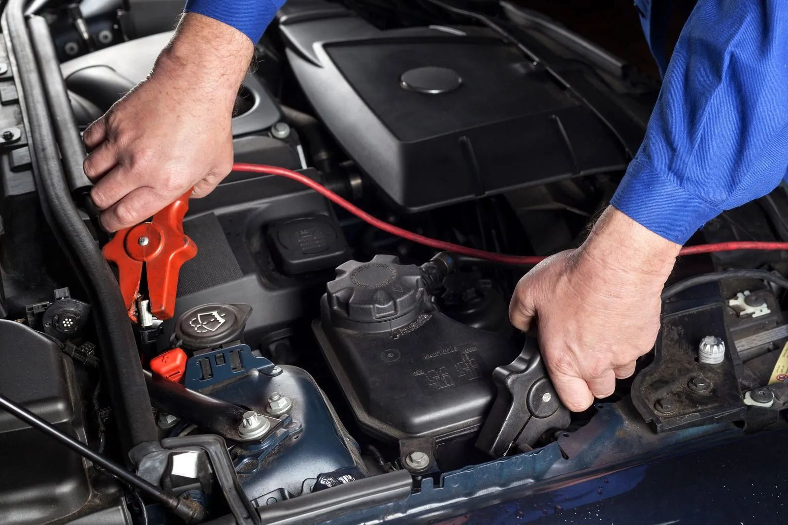 Hands using jumper cables to connect a car battery in the engine bay