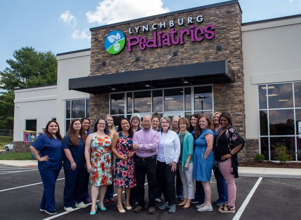 A large group of staff posing for a photo in front of the Lynchburg Pediatrics building on a sunny day.