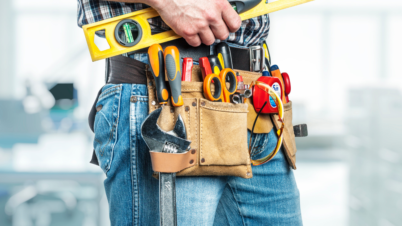 Close-up of a worker’s tool belt with pliers, screwdriver, tape measure, and drill on jeans
