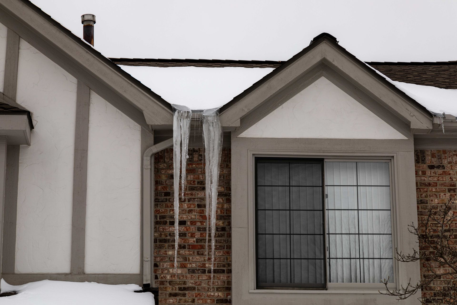 Long icicles spill from roof valleys, indicating ice dam buildup and potential roof damage. Long icicles spill from roof valleys, indicating ice dam buildup and potential roof damage.