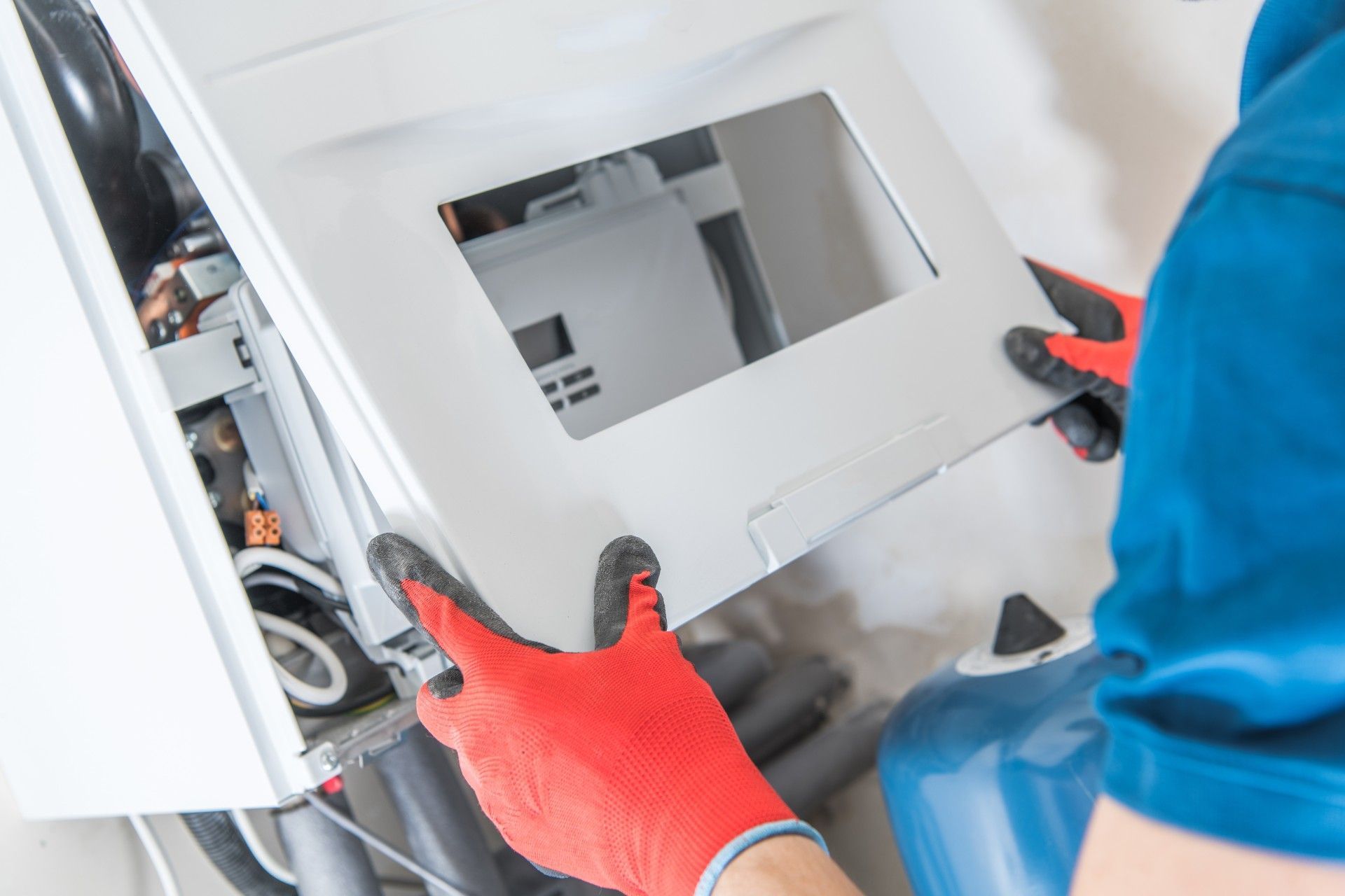 A man wearing red gloves is working on a boiler.