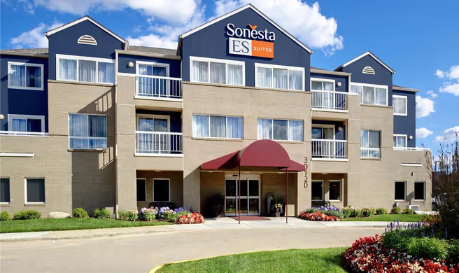 Sonesta ES Suites hotel in warren, michigan exterior with beige facade, blue roof accents, and red awning at entrance