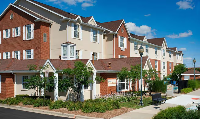 Modern apartment buildings with brick and beige siding, balconies, and landscaped sidewalk under a blue sky